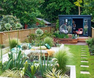 A small rectangular back garden divided into areas using raised beds and planting with a summer house at the end of the garden