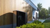 A grey and black Daikin heat pump up against a wooden exterior of a house