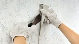 Hands removing wallpaper with a scraper