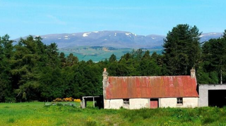 A hillside property in green fields with views of surrounding countryside with a small hut like property and garage